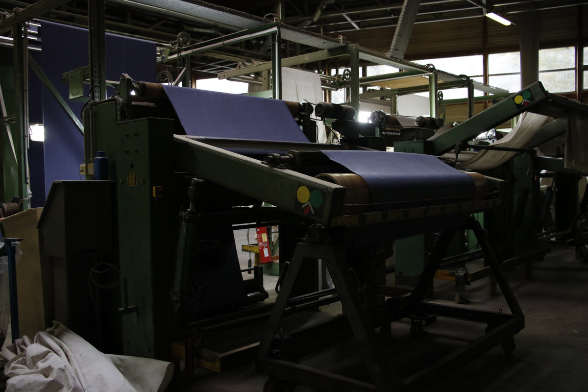 Du tissu bleu passe entre les rouleaux d’une machine textile